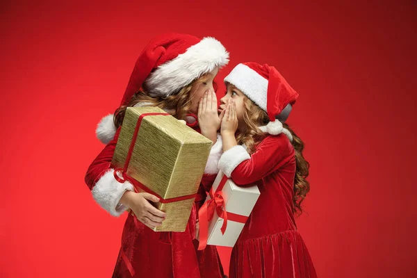 Duas meninas felizes em chapéus de Papai Noel com caixas de presente no estúdio — Fotografia de Stock