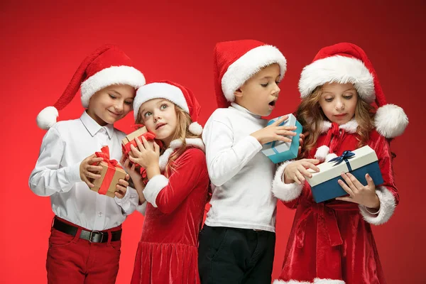 Две счастливые девочки и мальчики в шляпах Санта-Клауса с подарочными коробками в студии — стоковое фото