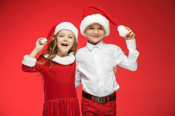 Dois meninos e meninas felizes em chapéus de Papai Noel com caixas de presente no estúdio — Fotografia de Stock