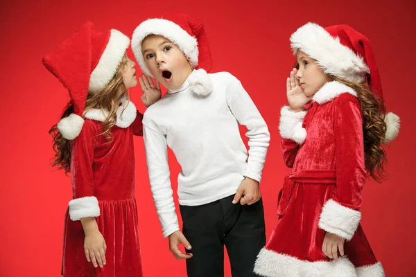 O menino feliz e as meninas em chapéus de Papai Noel com caixas de presente no estúdio — Fotografia de Stock