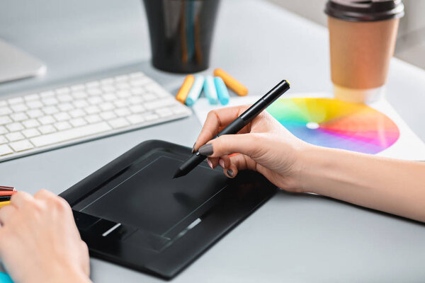 The gray desk with laptop, notepad with blank sheet, pot of flower, stylus and tablet for retouching