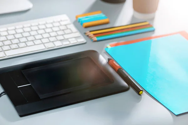 A mesa cinza com laptop, bloco de notas com folha em branco, vaso de flor, estilete e tablet para retoque — Fotografia de Stock