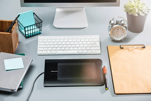 A mesa cinza com laptop, bloco de notas com folha em branco, vaso de flor, estilete e tablet para retoque — Fotografia de Stock