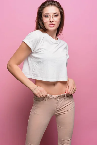 かなり若いセクシーなファッション官能的な女性が流行に敏感なスタイルのジーンズを着たピンクの背景にポーズ — ストック写真
