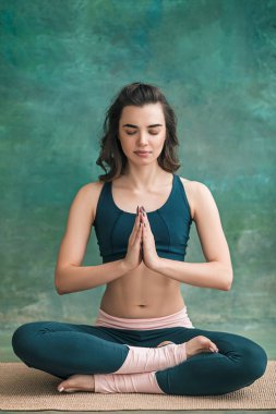 Genç bir kadının yeşil arka plan üzerinde yoga egzersizleri yapması stüdyo çekim