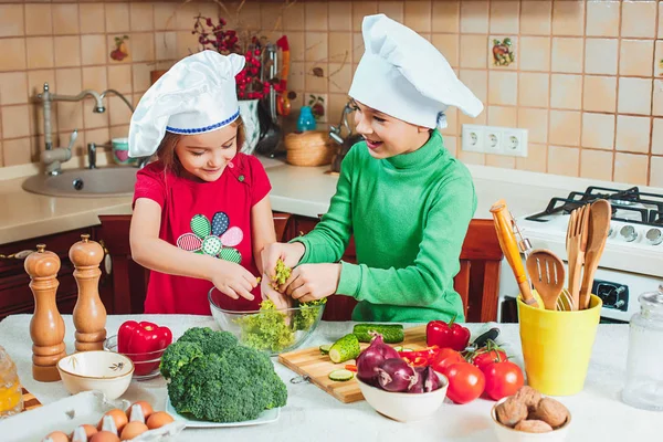 面白い子供たちを準備している幸せな家族、キッチンで新鮮な野菜のサラダ ロイヤリティフリーのストック画像
