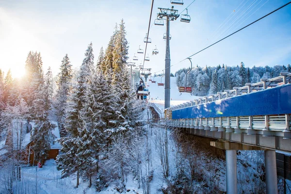 Skiers on the ski lift riding up at ski resort with beautiful background of snow-covered slopes, forests, hills in Bukovel, Ukraine — Stock Photo, Image