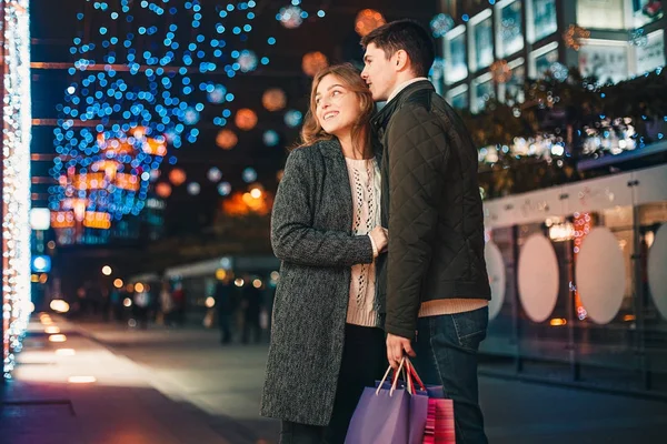 O casal feliz com sacos de compras desfrutando da noite no fundo da cidade — Fotografia de Stock