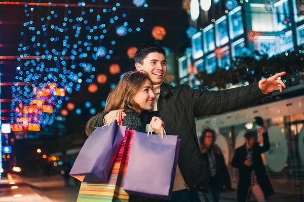 Das glückliche Paar mit Einkaufstüten genießt die Nacht im Hintergrund der Stadt — Stockfoto