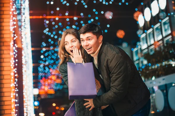 O casal feliz com sacos de compras desfrutando da noite no fundo da cidade — Fotografia de Stock