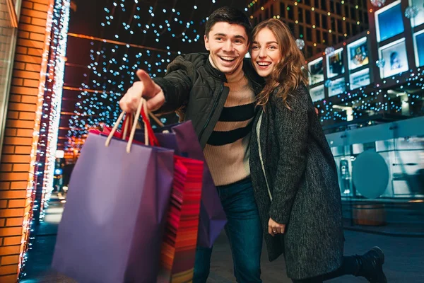 Das glückliche Paar mit Einkaufstüten genießt die Nacht im Hintergrund der Stadt — Stockfoto