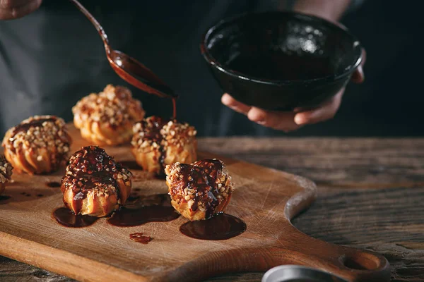 Decorating delicious homemade eclairs with chocolate and peanuts — Stock Photo, Image