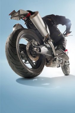 Motorcu siyah ceket ve sportif bisikletini mavi zemin üzerine oturan kask