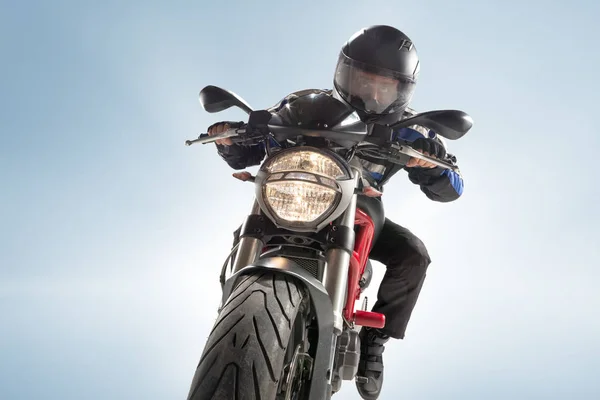 Байкер в черной куртке и шлеме сидит на спортивном велосипеде на синем фоне — стоковое фото