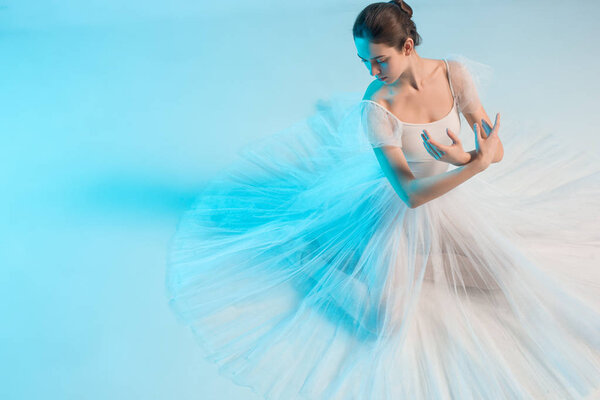 Young and incredibly beautiful ballerina is posing and dancing in a blue studio