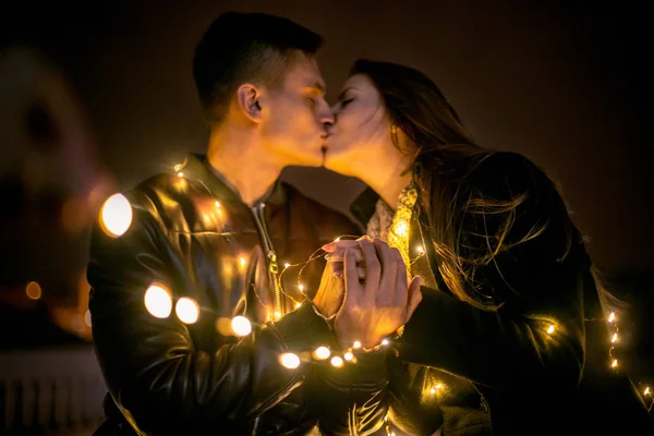 Pareja joven besándose y abrazándose al aire libre en la calle de la noche en Navidad —  Fotos de Stock