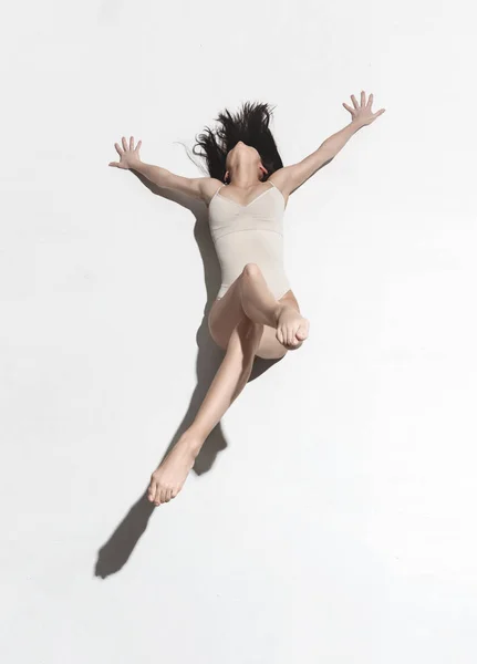 Young beautiful dancer in beige dress dancing on gray background