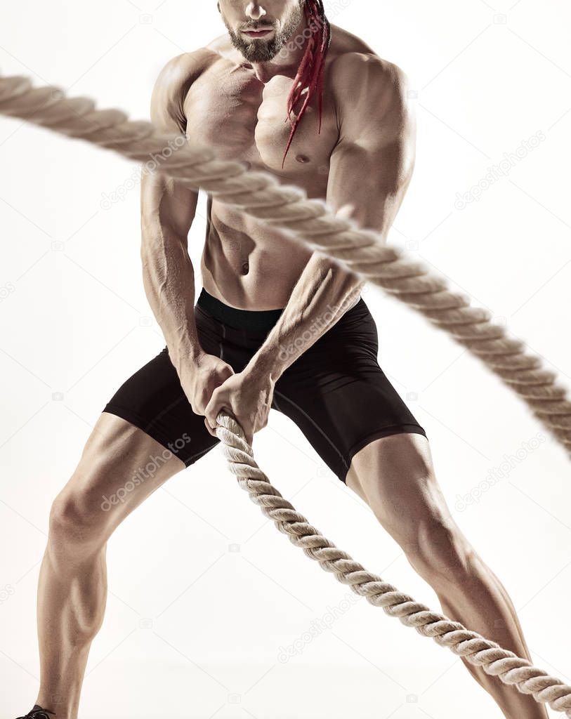 Attractive muscular man working out with heavy ropes.