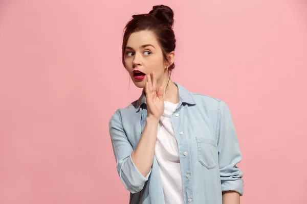 The young woman whispering a secret behind her hand over pink background — Stock Photo, Image