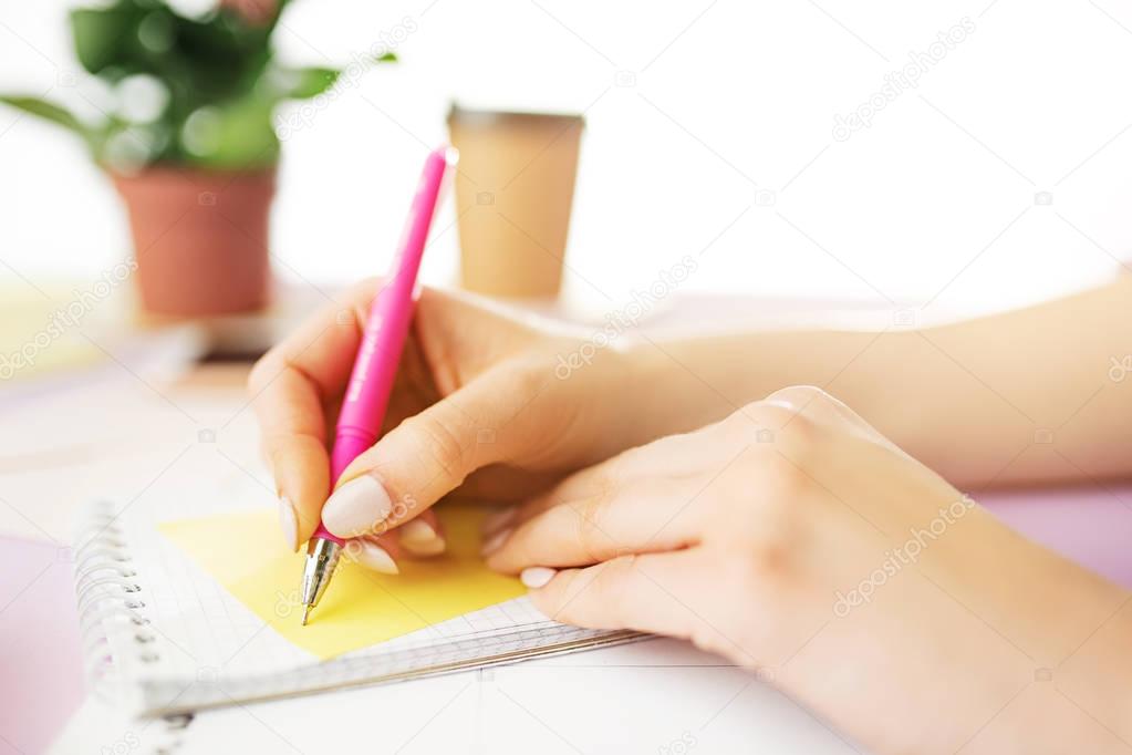 The female hands holding pen. The phone on trendy pink desk.