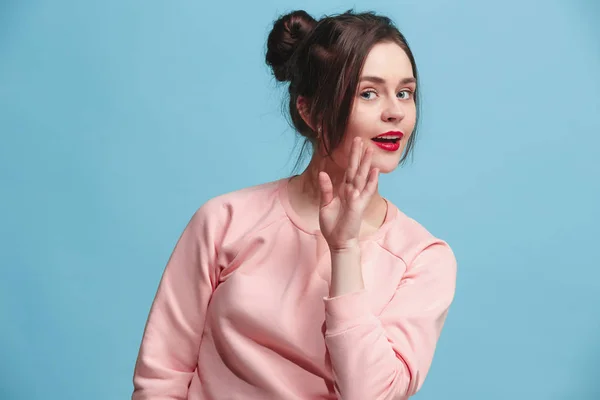 The young woman whispering a secret behind her hand over blue background — Stock Photo, Image