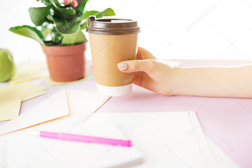 The female hands holding coffee on trendy pink desk.