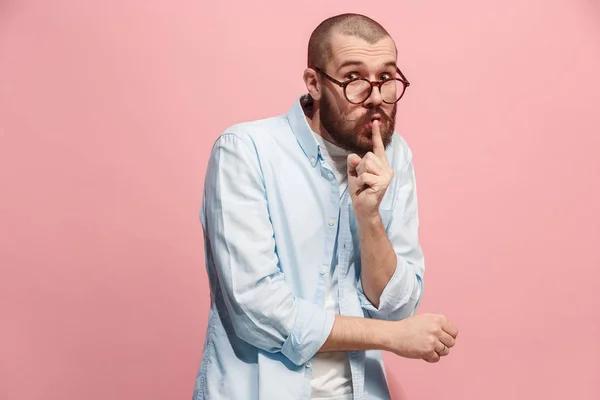 Der junge Mann flüstert ein Geheimnis hinter ihrer Hand über rosa Hintergrund — Stockfoto