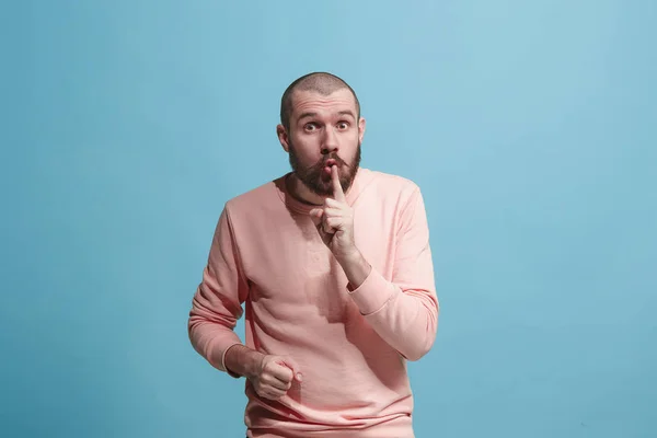 Der junge Mann flüstert ein Geheimnis hinter ihrer Hand vor blauem Hintergrund — Stockfoto