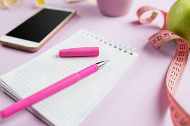 Yeşil elma, bant, cep telefonu, kalem ve açık defter ölçme yan görünüm. Fitness kavramı.
