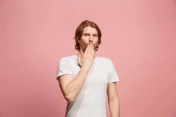 Il giovane uomo sussurrando un segreto dietro la sua mano su sfondo rosa — Foto Stock