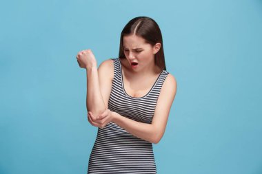 The elbow ache. The sad woman with elbow ache or pain on a blue studio background.
