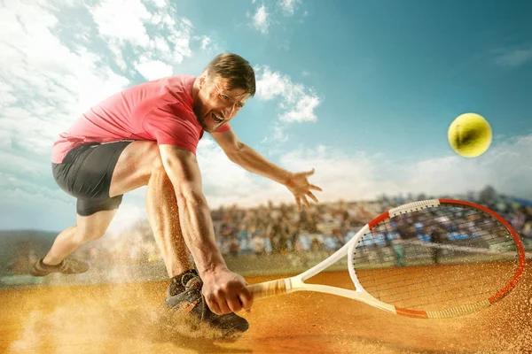 O jogador que salta, homem em forma caucasiano, a jogar ténis na quadra de barro com espectadores — Fotografia de Stock