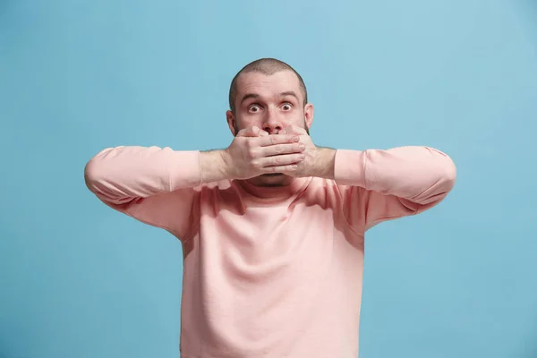 Der junge Mann flüstert ein Geheimnis hinter ihrer Hand vor blauem Hintergrund — Stockfoto