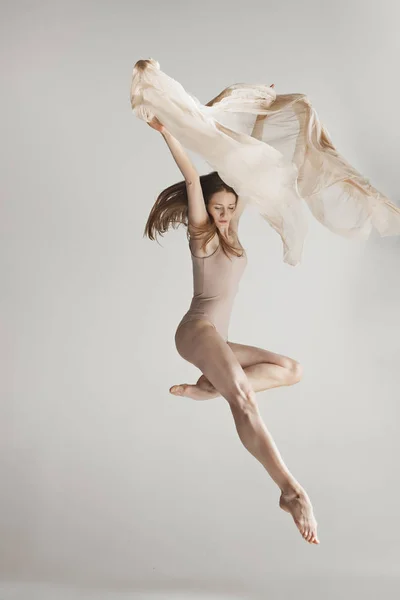 Joven hermosa bailarina en traje de baño beige bailando sobre fondo gris —  Fotos de Stock