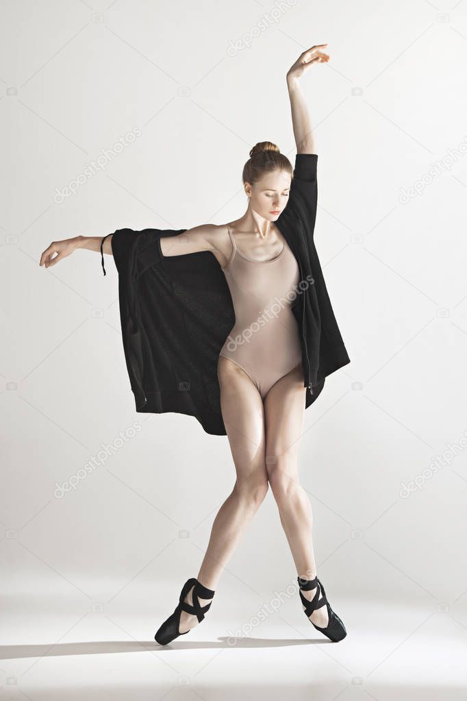 Young beautiful dancer in beige swimsuit dancing on gray background