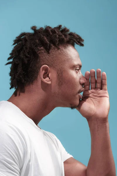 The young Afro-American man whispering a secret behind her hand over blue background