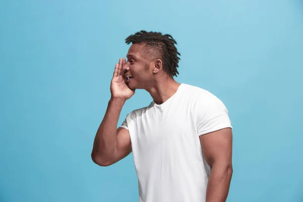 O jovem afro-americano sussurrando um segredo atrás de sua mão sobre fundo azul — Fotografia de Stock