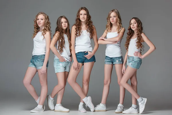 The fashion girls standing together and looking at camera over gray studio background — Stock Photo, Image