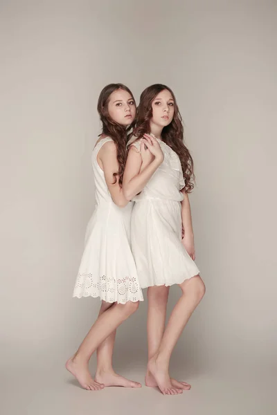 The fashion girls standing together and looking at camera over gray studio background — Stock Photo, Image