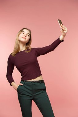 Şirin esmer kız bir selfie alır. O yaygın gülümsüyor. Uzun dalgalı esmer saçları. Güzellik kız pembe arka plan üzerinde.