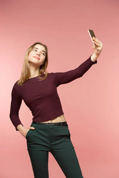 Schattige brunette meisje neemt een selfie. Ze glimlacht wijd. Ze heeft lang golvend brunette haar. Schoonheid meisje op de roze achtergrond. — Stockfoto