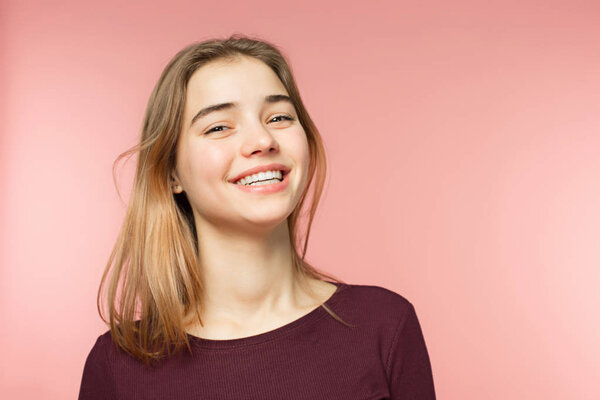 Женщина улыбается с идеальной улыбкой и белыми зубами на розовом фоне студии и смотрит в камеру
