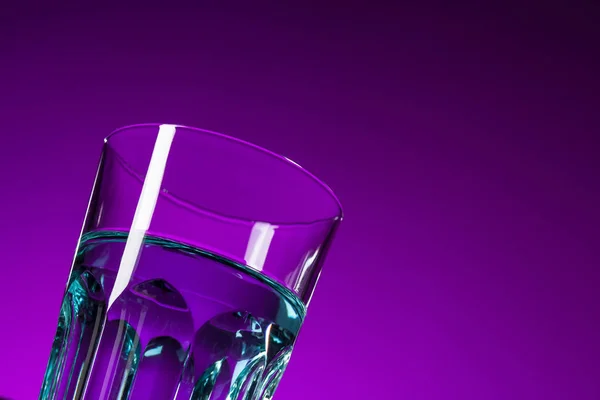 El agua en vidrio sobre fondo lila —  Fotos de Stock