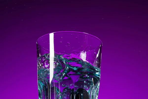 Das Wasser plätschert im Glas auf fliederfarbenem Hintergrund — Stockfoto