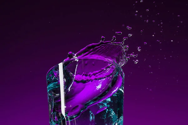 Das Wasser plätschert im Glas auf fliederfarbenem Hintergrund — Stockfoto