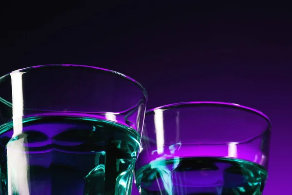Das Wasser in zwei Glasscheiben auf fliederfarbenem Hintergrund — Stockfoto