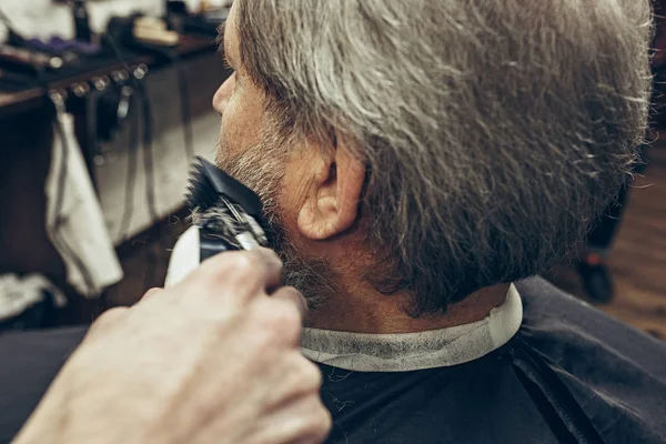 Närbild sida bakifrån stilig senior skäggiga kaukasiska man få skägg grooming i modern barbershop. — Stockfoto