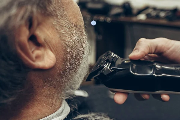Close-up lado trasero ver guapo mayor barbudo caucásico hombre consiguiendo barba aseo en moderno barbería . —  Fotos de Stock