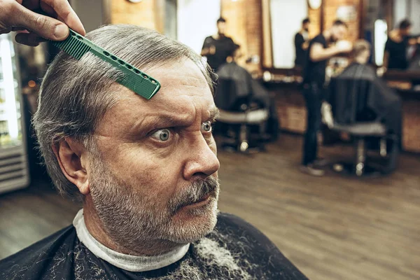 The hands of barber making haircut attractive old man in barbershop