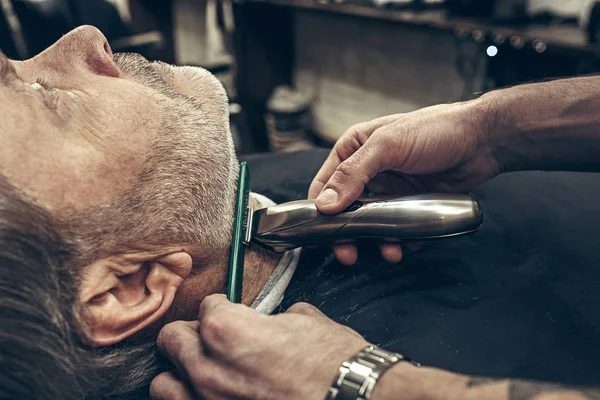 Крупним планом вид збоку портрет красивого старшого бородатого білого чоловіка, який доглядає за бородою в сучасному перукарні . — стокове фото